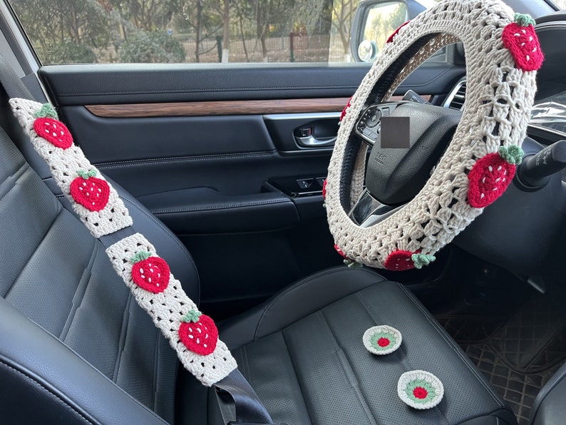 May include: A white crocheted steering wheel cover with red strawberry designs. The cover is also available in seatbelt covers and small coasters with the same design.
