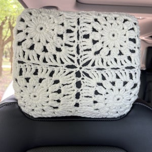 May include: White crocheted headrest cover with a square pattern. The cover is made of a soft, white yarn and has a delicate, floral design.