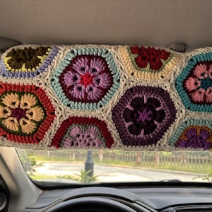 Könnte beinhalten: Ein mehrfarbiger, gehäkelter Sonnenblendenbezug mit einem Patchwork-Design aus sechseckigen Formen. Die Häkelarbeit verwendet verschiedene Farben, darunter Lila, Rot, Grün und Blau, wodurch ein lebendiges und strukturiertes Aussehen entsteht. Die Sonnenblende ist in einem Auto installiert.