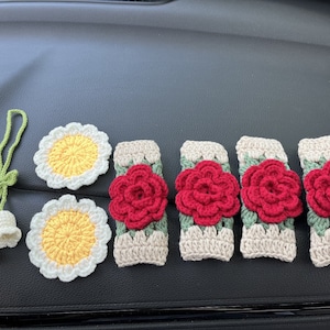 May include: Five crocheted rose-shaped car air freshener ornaments in red and green, with two crocheted daisy-shaped ornaments in white and yellow.