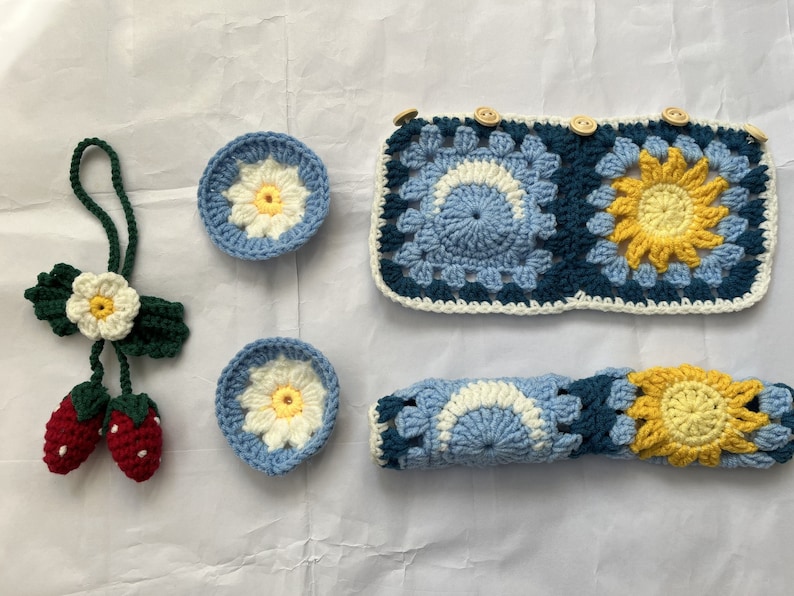 May include: A set of crocheted items in blue, yellow, and white. The set includes a coaster, a headband, and a small flower-shaped keychain.
