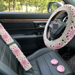 K&ouml;nnte beinhalten: Ein Set an geh&auml;kelten Autozubeh&ouml;r in Rosa und Wei&szlig;. Das Set beinhaltet eine Lenkradabdeckung, Sicherheitsgurtbez&uuml;ge und zwei kleine rosa geh&auml;kelte Kreise.