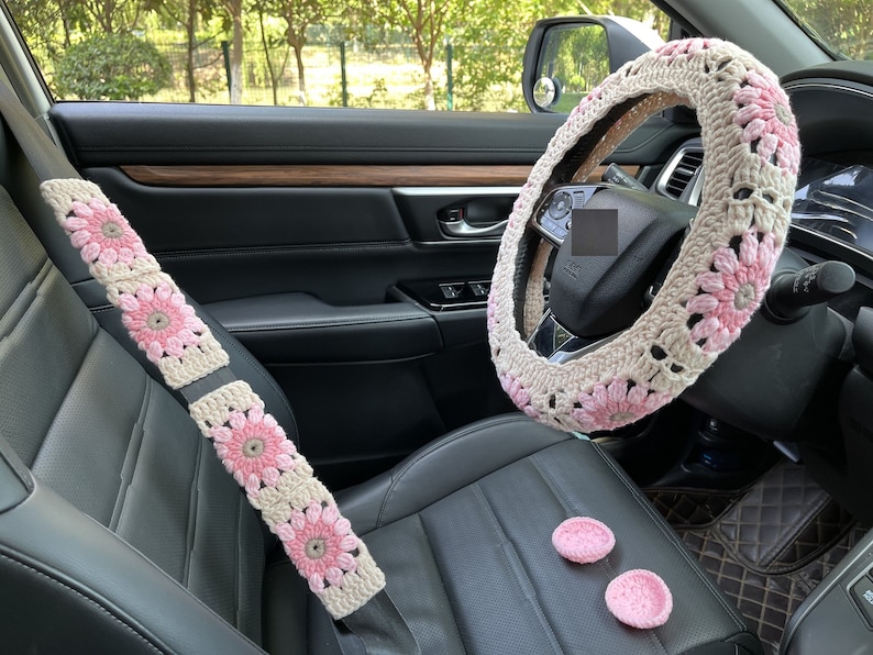 K&ouml;nnte beinhalten: Ein Set an geh&auml;kelten Autozubeh&ouml;r in Rosa und Wei&szlig;. Das Set beinhaltet eine Lenkradabdeckung, Sicherheitsgurtbez&uuml;ge und zwei kleine rosa geh&auml;kelte Kreise.