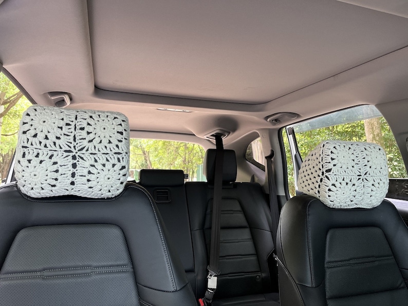 May include: White crocheted headrest covers for car seats. The covers are made of a delicate, lacy pattern and are placed on the headrests of the back seats of a car.
