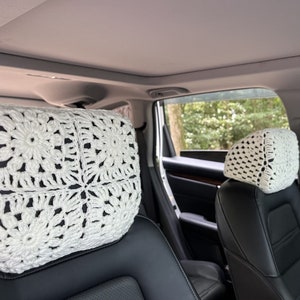 May include: Two white crocheted headrest covers for car seats. The covers are made with a square pattern and feature a delicate floral design.