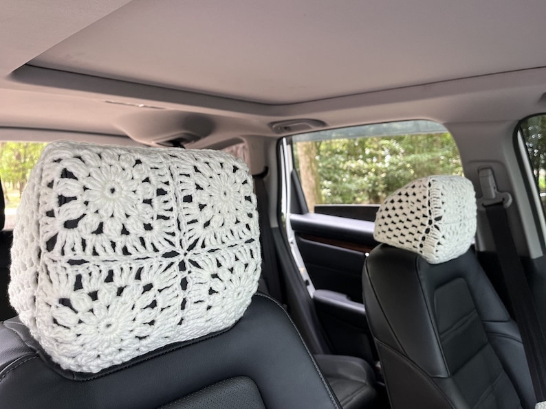 May include: Two white crocheted headrest covers for car seats. The covers are made with a square pattern and feature a delicate floral design.