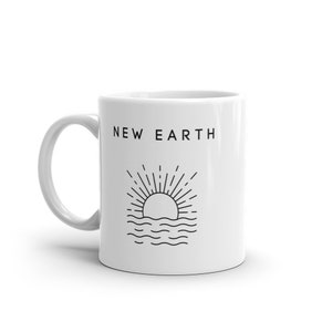 Puede incluir: Taza de cerámica blanca con la inscripción "NEW EARTH" y un gráfico negro de un sol saliendo sobre el agua. La taza tiene un asa curva y es adecuada para bebidas frías o calientes.
