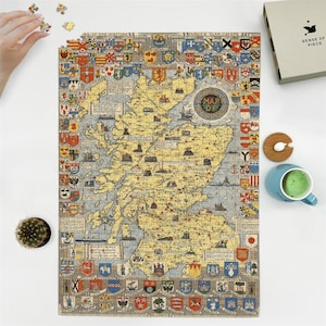 May include: A completed jigsaw puzzle depicting a vintage map of Scotland, featuring detailed illustrations and heraldic crests. The puzzle is mostly yellow and blue, with a circular "Map of" emblem. A hand is placing a puzzle piece.