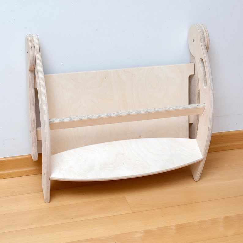 May include: A light wood bookshelf with two shelves and a curved bottom. The bookshelf is made of plywood and has a natural finish.