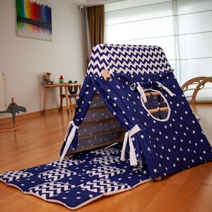 Puede incluir: Una tienda de campaña de juego azul y blanca con un patrón de estrellas y una pequeña ventana. La tienda tiene una alfombra con estampado de chevron blanco.