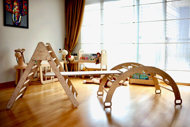 May include: Wooden playset for children, featuring a climbing triangle with a slide, a bridge, and a curved climbing arch. The set is made of natural wood and has a light brown finish.