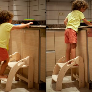May include: Two children stand on wooden step stools in a kitchen. The step stools are made of natural wood and have two steps. The children are wearing casual clothing.