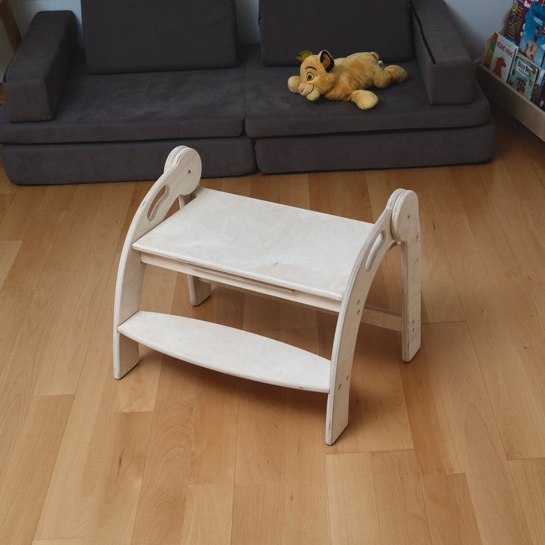 May include: A white wooden children's table and chair set with a step stool. The table has a smooth surface and rounded edges. The chair has a curved back and a step stool with a rounded edge.