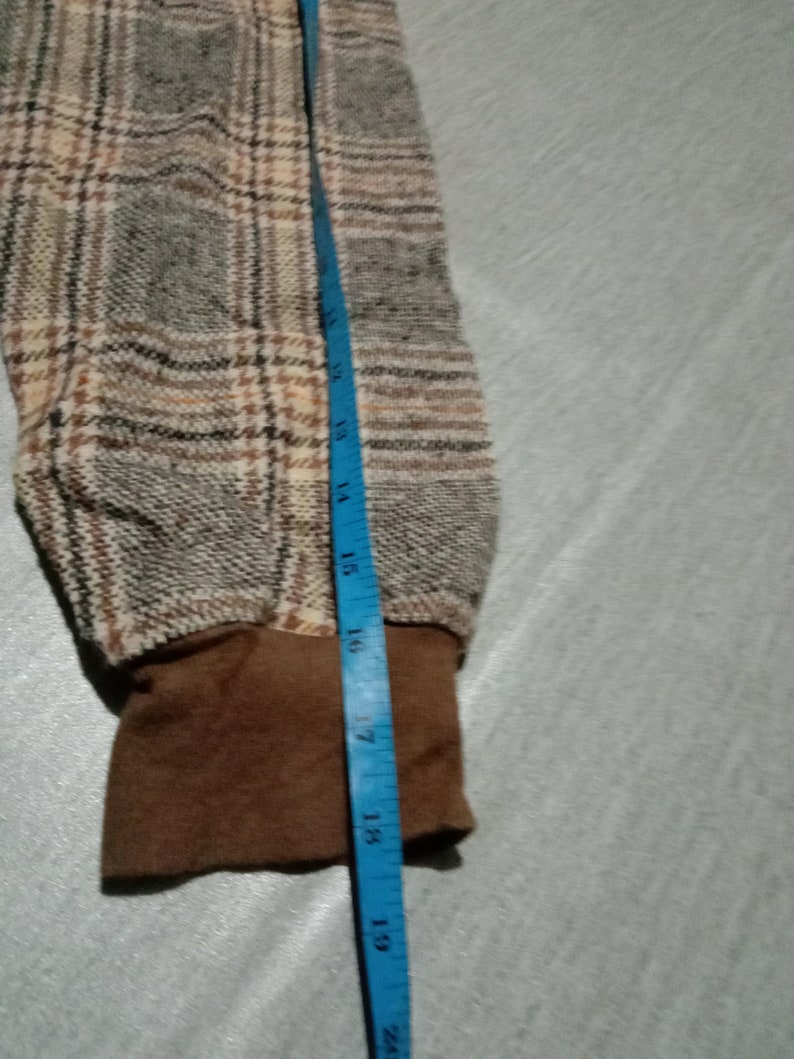 May include: Close-up of a brown and beige plaid fabric with a brown cuff. A blue measuring tape is visible along the right edge of the image, with the numbers 14 to 20 inches visible.