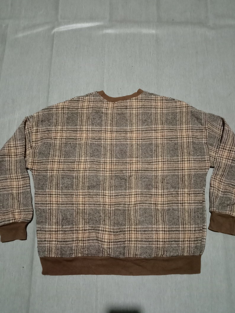 May include: A brown and beige plaid sweater with a brown ribbed collar and cuffs.