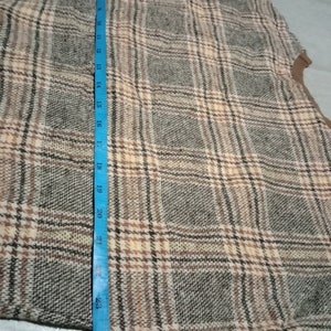 May include: A brown, beige, and black plaid fabric with a blue measuring tape along the left side. The tape measures 25 inches.