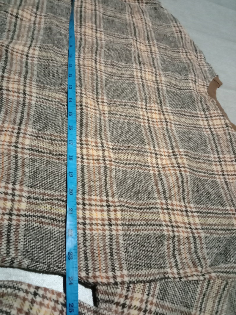 May include: A brown, beige, and black plaid fabric with a blue measuring tape along the left side. The tape measures 25 inches.