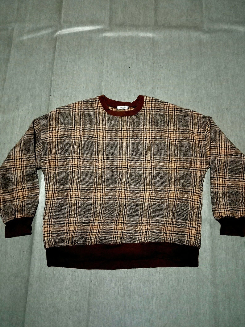 May include: A brown, beige, and black plaid sweater with a maroon ribbed collar and cuffs.