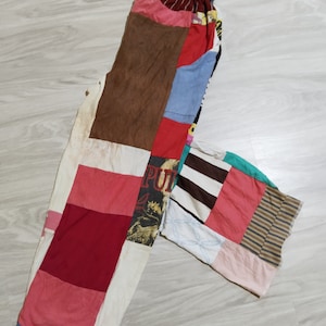 Op de afbeelding: Patchwork broek gemaakt van verschillende stoffen in verschillende kleuren, waaronder rood, bruin, blauw, wit en roze. De broek heeft een gestreepte tailleband en een patchwork ontwerp.