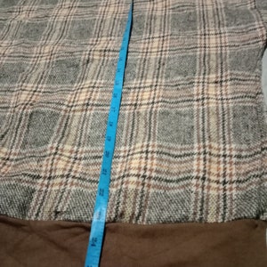 May include: Brown and beige plaid sweater with a brown ribbed hem. The sweater is measured with a blue tape measure.