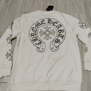 Op de afbeelding: Witte longsleeve trui met een zwart Chrome Hearts logo op de rug en kleinere logo's op de mouwen.