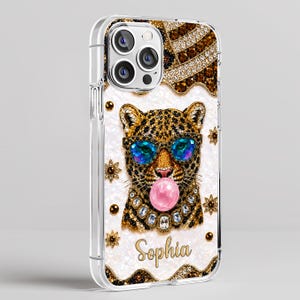 May include: A clear phone case featuring a leopard wearing blue-tinted sunglasses and blowing a pink bubblegum bubble. The leopard is adorned with gold and crystal accents, and the name Sophia is printed in gold script at the bottom of the case.