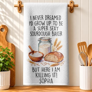 May include: A white waffle-weave kitchen towel featuring the text I NEVER DREAMED I'D GROW UP TO BE A SUPER SOURDOUGH BAKER BUT HERE I AM KILLING IT! SOPHIA, with a graphic of a glass jar, a wooden bowl of flour, and a loaf of bread.