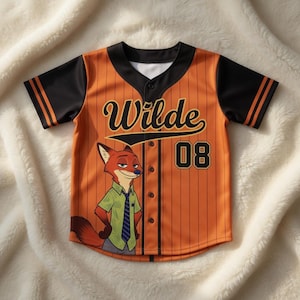 Puede incluir: Camiseta de b&eacute;isbol naranja con mangas y detalles en negro. Presenta el nombre "Wilde" y el n&uacute;mero "08" en negro. Un personaje de zorro de dibujos animados est&aacute; en la parte delantera. La camiseta tiene una botonadura.