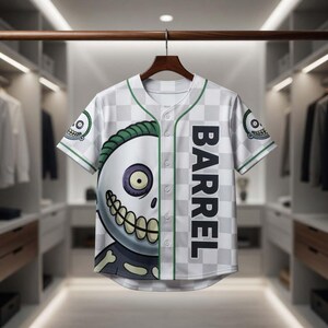 May include: White and gray baseball jersey with a checkerboard pattern and green trim. The jersey features a large cartoon skull graphic on the front and the word "BARREL" printed vertically. The sleeves have a small skull graphic.