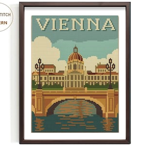 May include: Framed cross-stitch pattern featuring a pixelated illustration of Vienna, Austria. The artwork depicts a building with a dome, a bridge, and the word "VIENNA" in large letters. The frame is dark brown, and the background is white.