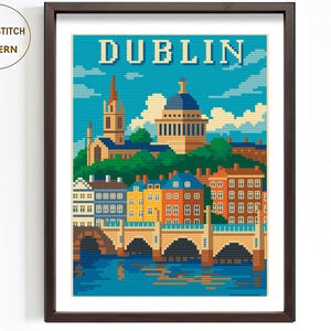 Puede incluir: Patrón de punto de cruz enmarcado con una colorida ilustración pixelada de Dublín, Irlanda. La obra de arte representa edificios, puentes y un río bajo un cielo azul. La palabra "DUBLIN" está en la parte superior.