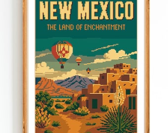 May include: A framed cross-stitch pattern featuring a New Mexico landscape. The artwork displays the text "NEW MEXICO" and "THE LAND OF ENCHANTMENT" above a scene with hot air balloons, mountains, and adobe buildings. The color palette includes shades of green, orange, and brown.
