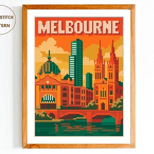 May include: A framed cross-stitch pattern depicting Melbourne, Australia, in a pixelated style. The artwork shows the city's skyline, including buildings and bridges, with the word "MELBOURNE" above. The sky is orange.
