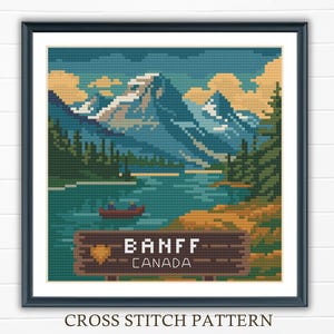 May include: Framed cross-stitch pattern showing a landscape of Banff, Canada. The image includes a lake, mountains, and a canoe. The sign reads "BANFF CANADA". The text "CROSS STITCH PATTERN" is at the bottom.