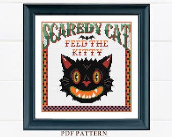 May include: A cross-stitch pattern featuring a black cat with a toothy grin and the text "Scaredy Cat Feed the Kitty". The pattern is framed in a black frame with a white background.