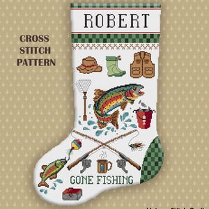 May include: A white cross stitch pattern of a Christmas stocking featuring the name ROBERT at the top. The design includes fishing gear, a large rainbow trout, a red bucket, two crossed fishing rods, and the text GONE FISHING at the bottom.