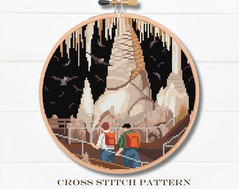 May include: Cross stitch pattern of a cave with stalactites and stalagmites. Two people are standing on a platform looking at the cave formations. The pattern is in a round hoop.