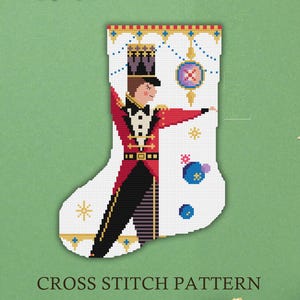 May include: A white Christmas stocking cross stitch pattern featuring a soldier in a red coat and black pants. The stocking has a decorative top with gold and blue accents, and the text "CROSS STITCH PATTERN" is at the bottom.