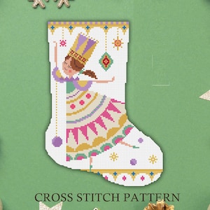Puede incluir: Un patrón de punto de cruz de calcetín navideño blanco con una bailarina con un vestido y una corona coloridos. El diseño incluye detalles en rosa, amarillo, morado y verde, con el texto "CROSS STITCH PATTERN" en la parte inferior.