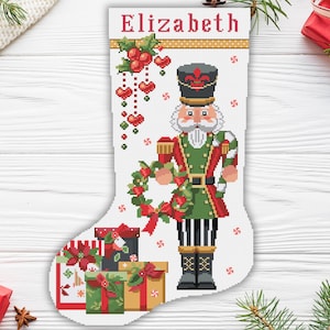 May include: A white Christmas stocking with a red and green nutcracker holding a wreath. The stocking has the name "Elizabeth" at the top and is decorated with red berries and hearts. The stocking is filled with wrapped gifts.
