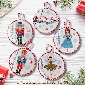May include: Set of five cross stitch patterns for Christmas ornaments featuring characters from The Nutcracker. The ornaments are round and feature a red and white border. The patterns include the Nutcracker, Clara, the Mouse King, Sugar Plum Fairy, and the Nutcracker with the text "Nutcracker" on the ornament.
