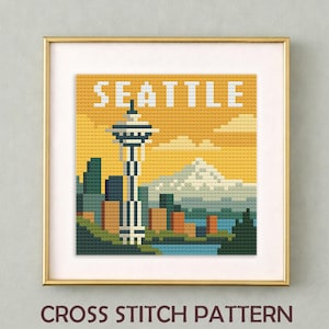 May include: Framed cross-stitch pattern featuring a Seattle cityscape with the Space Needle, mountains, and skyline. The word "SEATTLE" is stitched across the top. The text "CROSS STITCH PATTERN" is at the bottom. The artwork is in a gold frame.