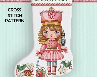 May include: A white Christmas stocking cross stitch pattern featuring a pink and gold nutcracker soldier design. The stocking has the name "Jennifer" at the top and the words "Cross Stitch Pattern" on the side. The bottom has holiday-themed cross stitch designs.