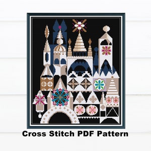 May include: A framed cross-stitch pattern featuring a colorful, stylized architectural design against a black background. The design includes geometric shapes in white, tan, blue, and gold. The text "Cross Stitch PDF Pattern" is at the bottom.