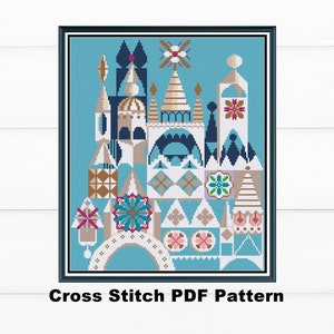 May include: A framed cross-stitch pattern featuring a whimsical architectural design in shades of blue, tan, and white. The image includes a variety of geometric shapes and floral accents. The text "Cross Stitch PDF Pattern" is at the bottom.