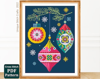 May include: Cross stitch pattern featuring three colorful Christmas ornaments with geometric designs hanging from a pine branch against a dark blue background. The ornaments are yellow, pink, and green with white snowflakes scattered around them.