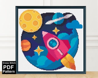 May include: A cross stitch pattern featuring a pink rocket ship flying through space with a yellow moon, blue and orange planets, and stars. The pattern is framed in a black frame.
