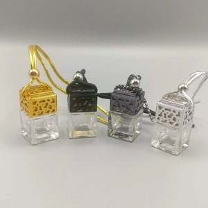 May include: Three glass car air fresheners with decorative metal tops. The air fresheners are gold, black, and silver. Each air freshener has a black string for hanging.