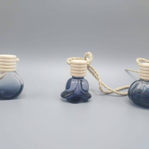 May include: Three glass car air fresheners with a blue gradient and white lids. Each air freshener is attached to a string.