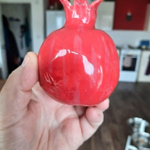May include: A bright red ceramic pomegranate figurine. The figurine is glossy and has a detailed design.